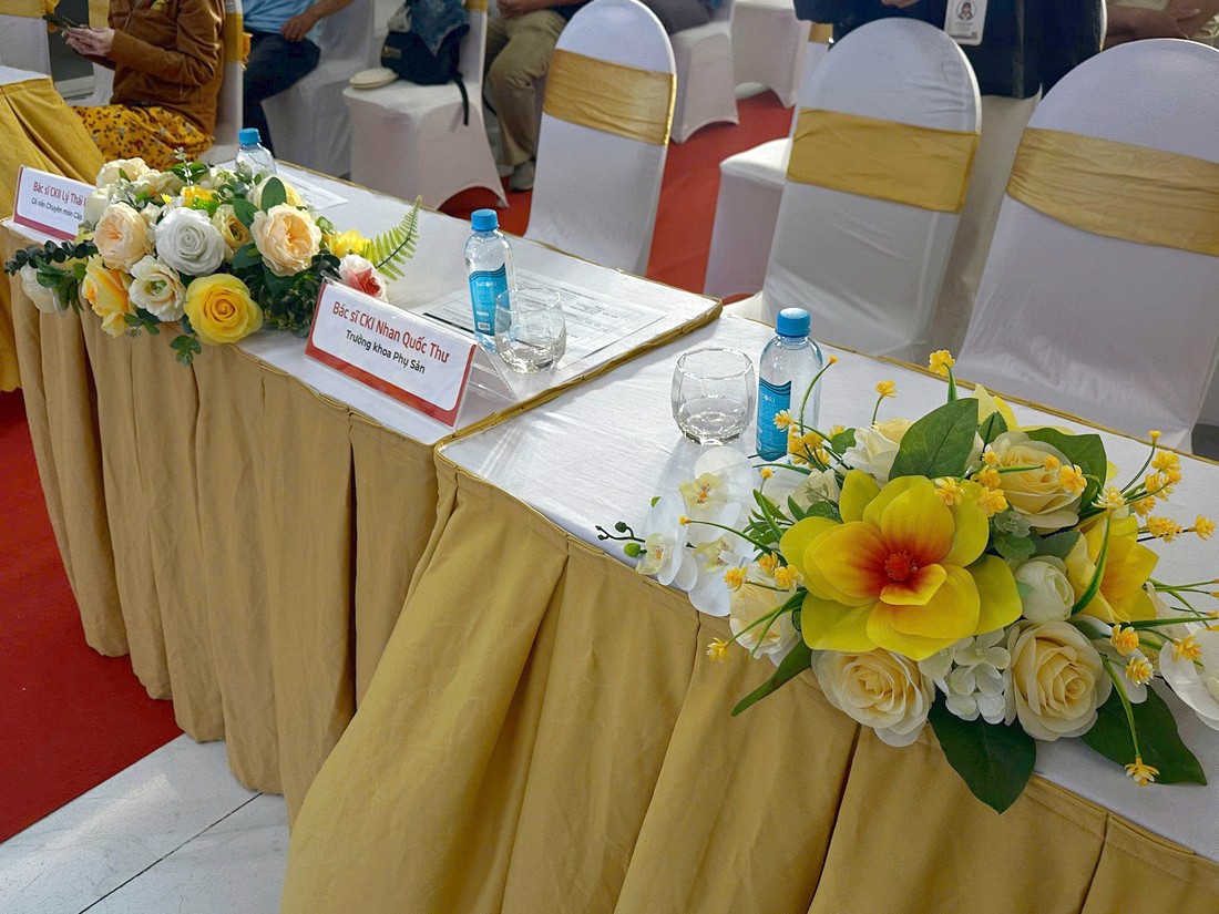 Bàn đại biểu phủ khăn trắng váy vàng và trang trí hoa tại tọa đàm y khoa