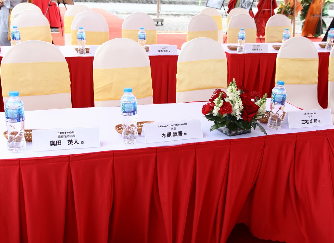 Sân khấu lễ động thổ QBB với backdrop in, bục phát biểu và khu vực xúc cát phía trước.