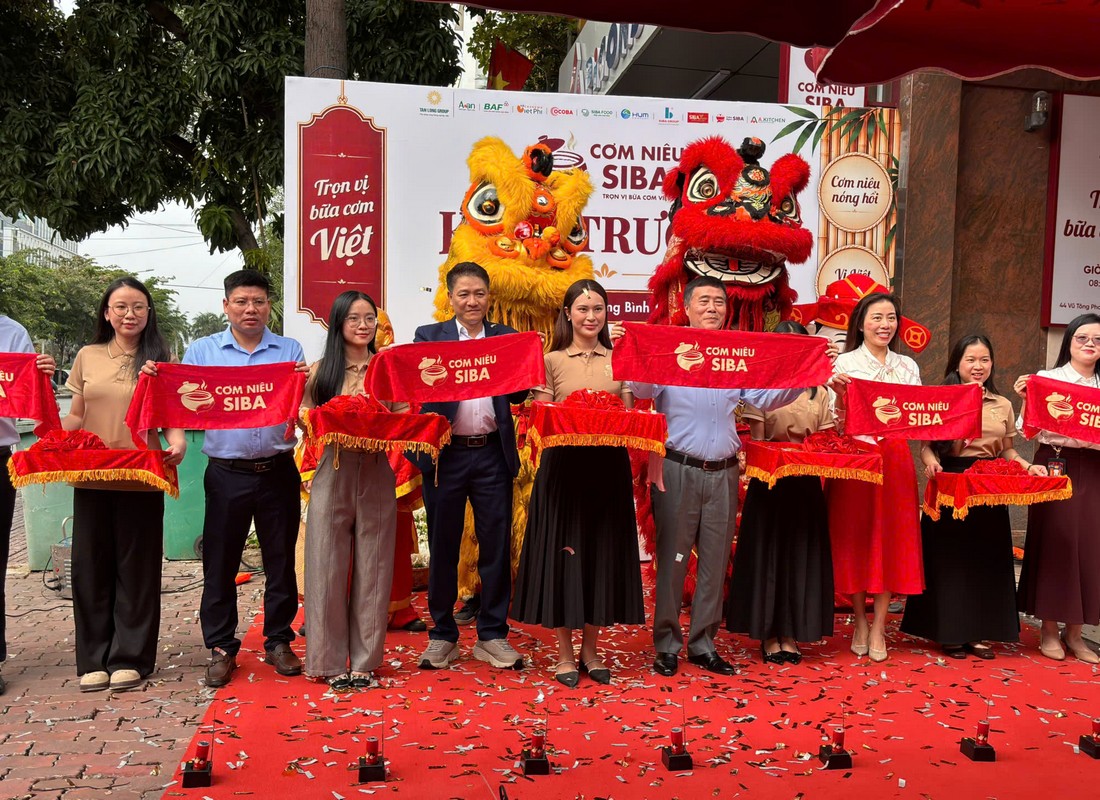 PG cầm khay nghi thức đứng cùng đại biểu trước backdrop khai trương Cơm Niêu SIBA.