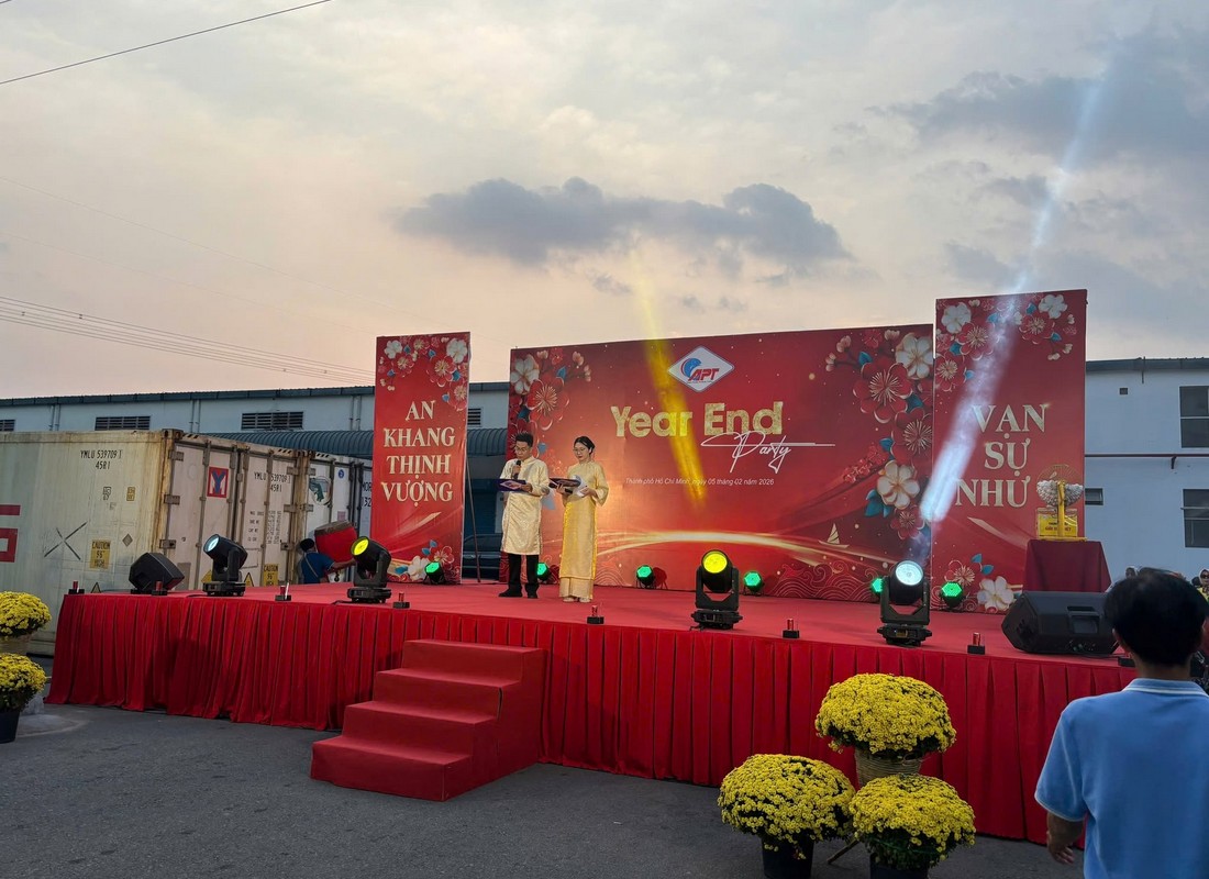 Hai MC mặc áo dài dẫn chương trình Year End Party APT trên sân khấu ngoài trời.